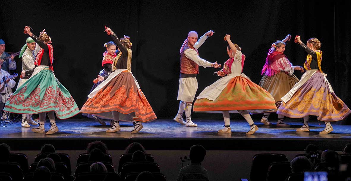 Grupo de coros y danzas bailando sobre el escenario con trajes tradicionales